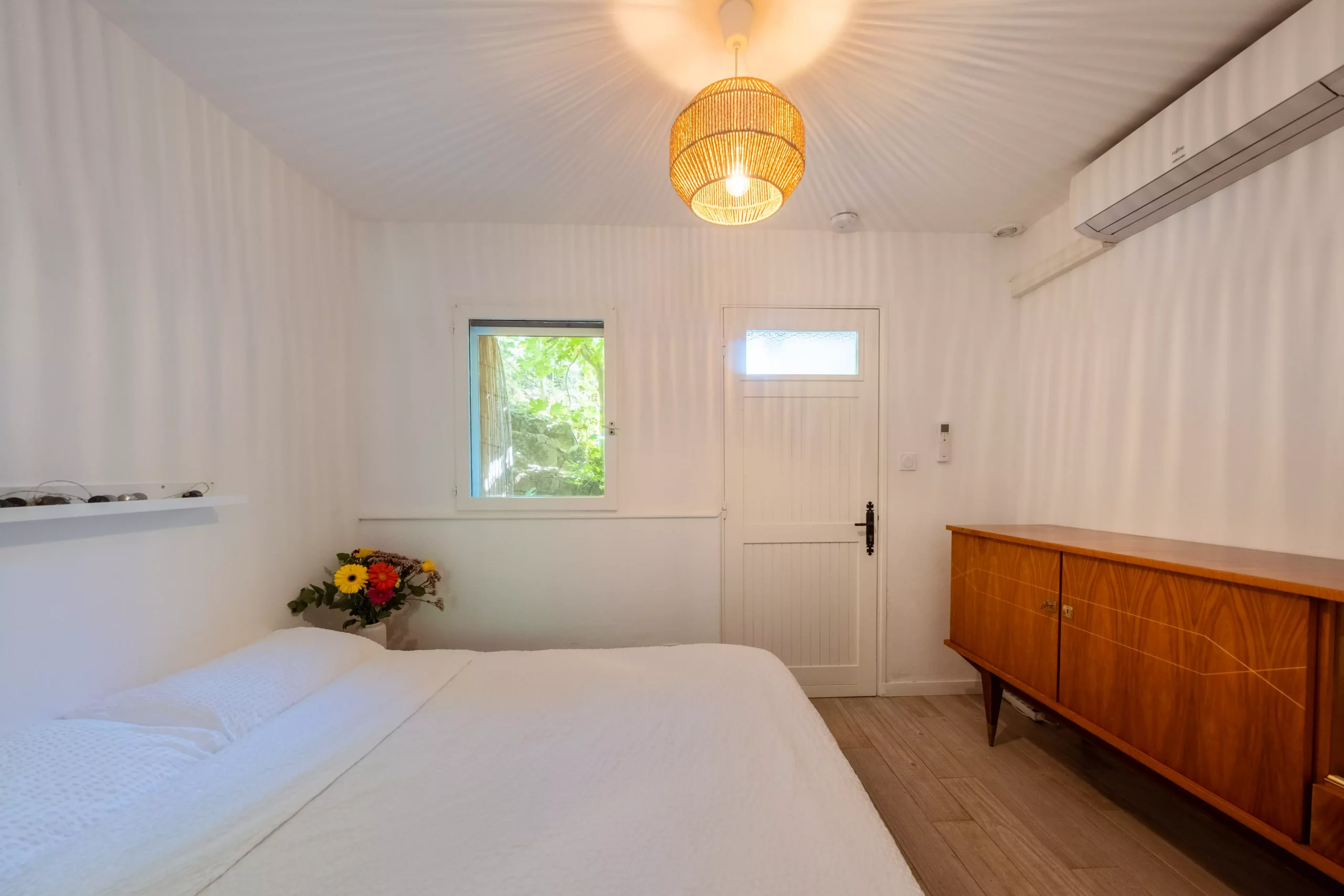 Villa Le Perchoir - Grand lit blanc, commode marron, bouquet de fleurs.